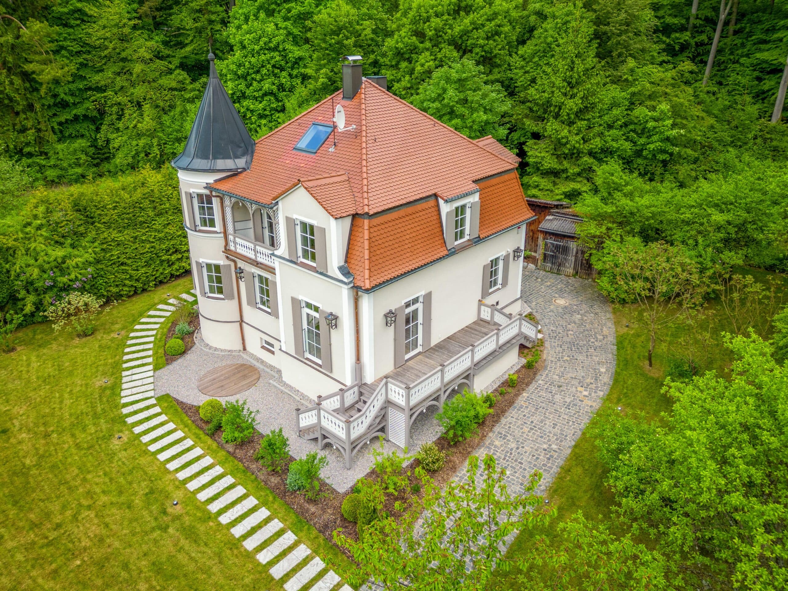 Vogelperspektive eines weißen Hauses mit rotem Dach und Gartenwegen in üppigem Grün.