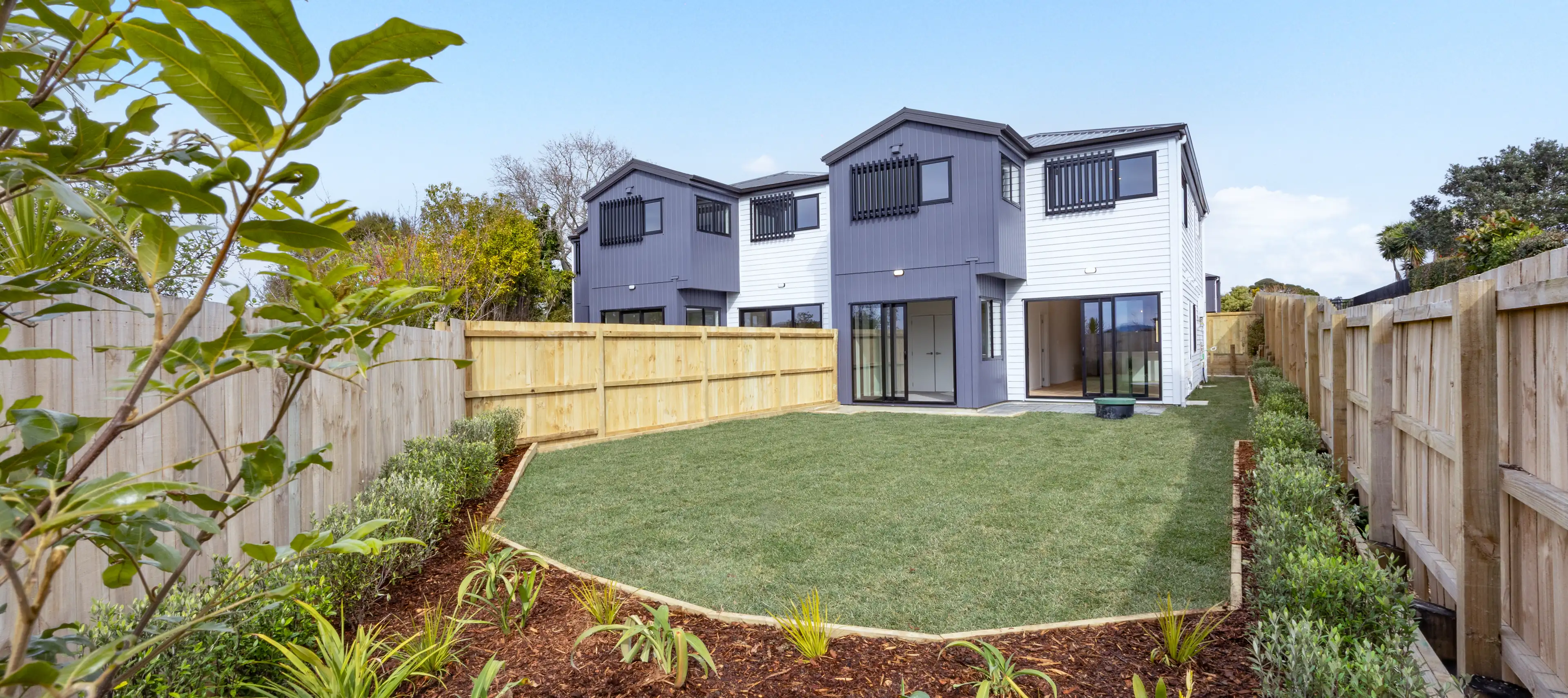 The Eden Group homes at 12-14 Taupo Street, Green Bay, in white weatherboard and grey vertical cladding with internal access garages.