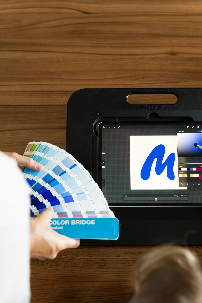 Twee medewerkers van brandlos maken samen een logo op de iPad. Een medewerker tekent op de iPad en de andere medewerker van Brandlos houdt een Pantone waaier vast