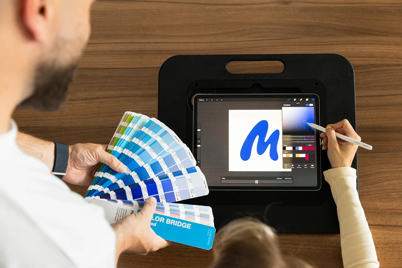 Twee medewerkers van brandlos maken samen een logo op de iPad. Een medewerker tekent op de iPad en de andere medewerker van Brandlos houdt een Pantone waaier vast