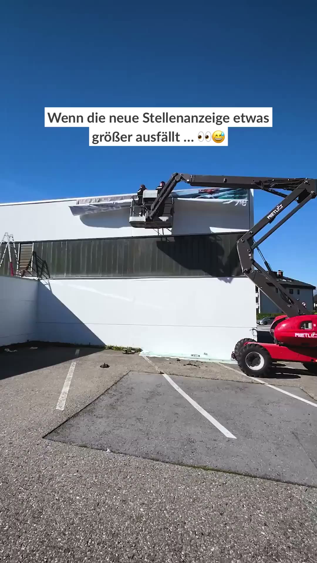 Mitarbeiter auf einer Hebebuehne montiert ein grosses Stellenanzeigen-Plakat an der Hallenwand