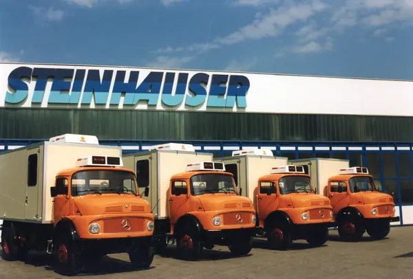 Vier orangefarbene Lkw mit Kofferaufbau vor dem Steinhauser-Gebäude