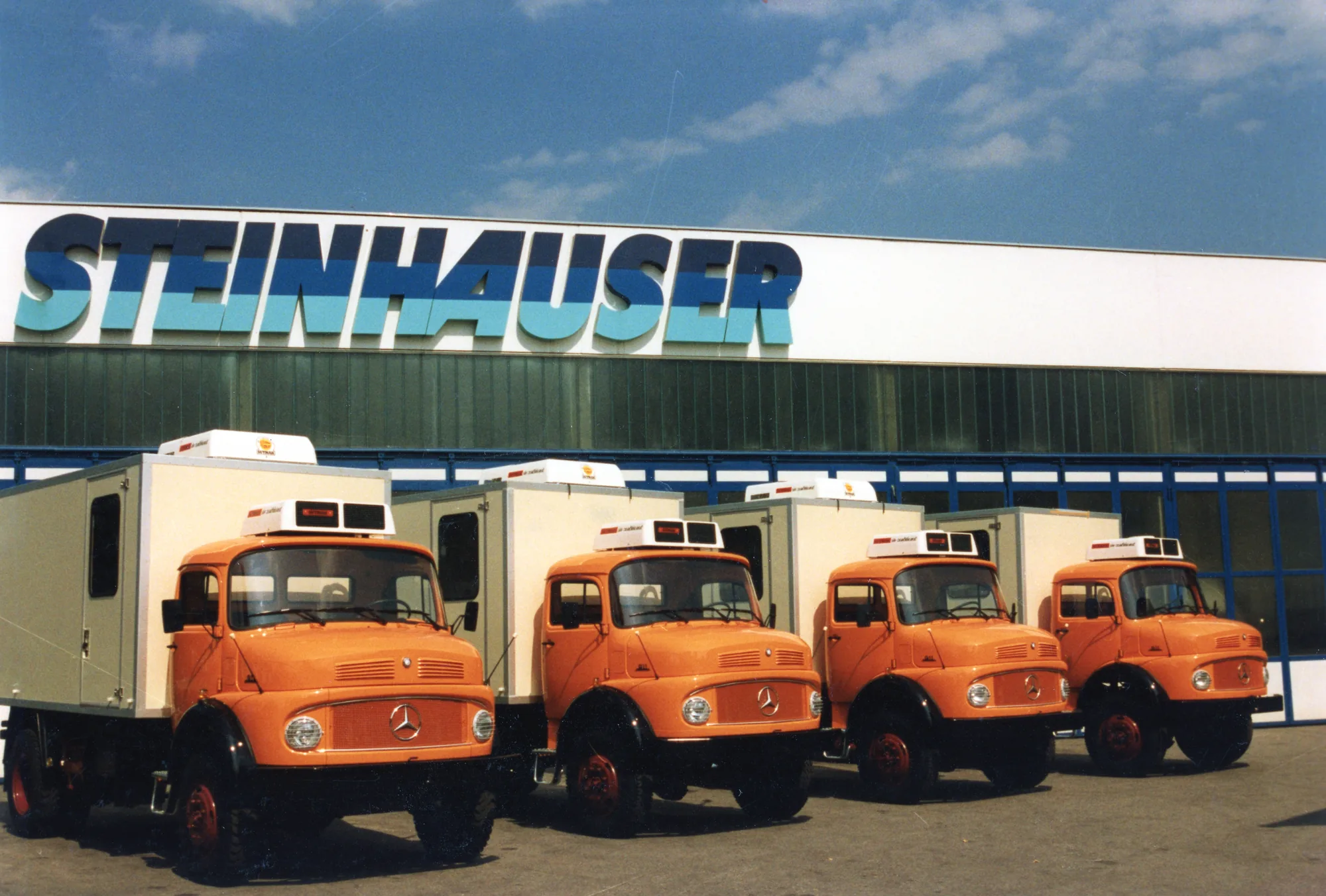 Vier orangefarbene Lkw mit Kofferaufbau vor dem Steinhauser-Gebäude