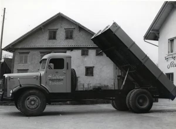 Kipper-Lkw mit angehobener Mulde vor einem Haus, Schwarzweiss