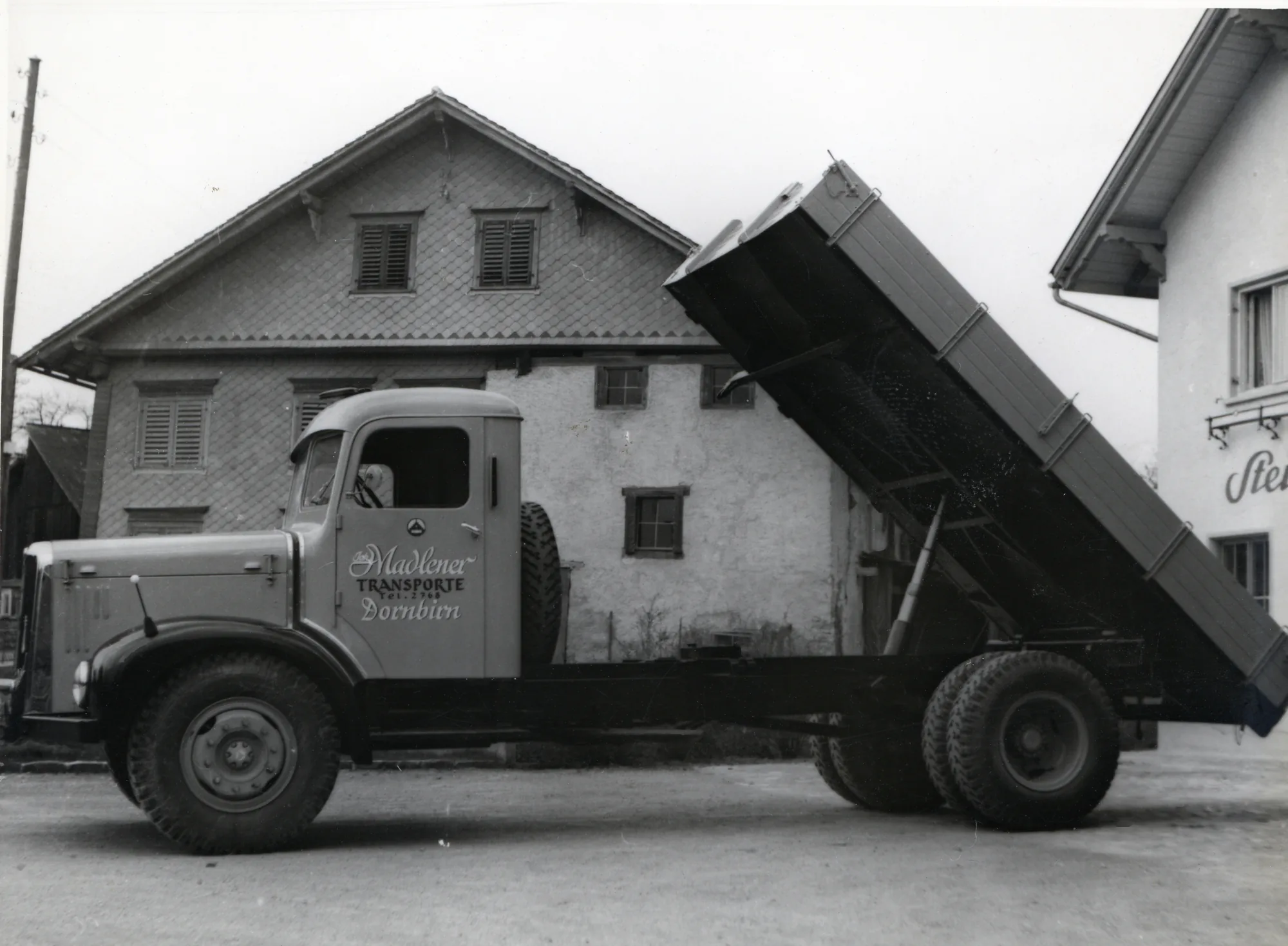 Kipper-Lkw mit angehobener Mulde vor einem Haus, Schwarzweiss