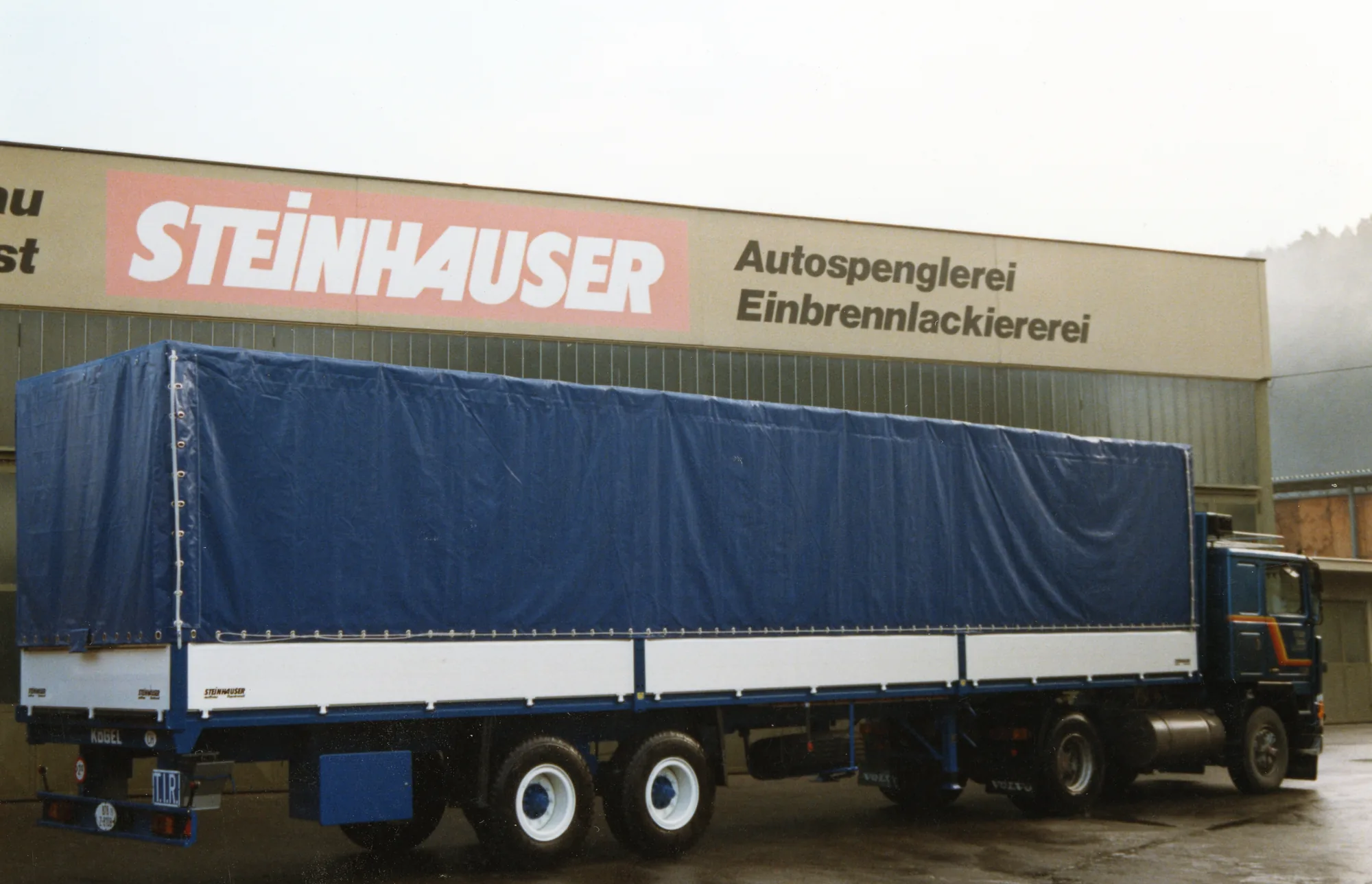 Sattelzug mit blauem Planenauflieger vor der Steinhauser-Autospenglerei