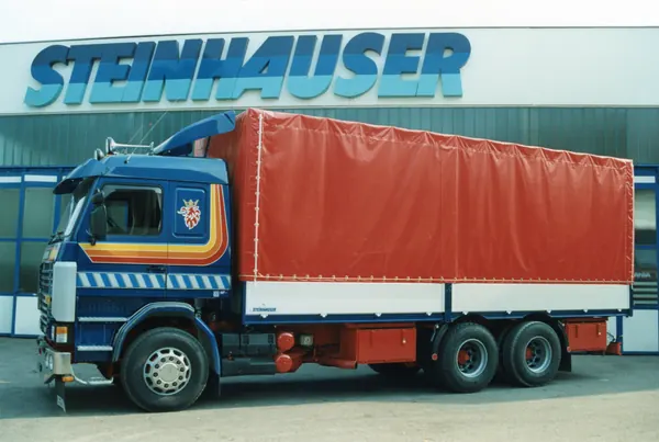 Scania-Dreiachser mit rotem Planenaufbau vor dem Steinhauser-Gebäude