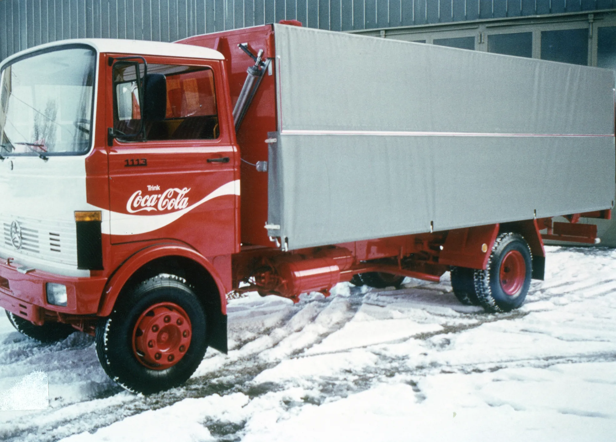 Roter Lkw mit Coca-Cola-Beschriftung und Pritschenaufbau im Schnee