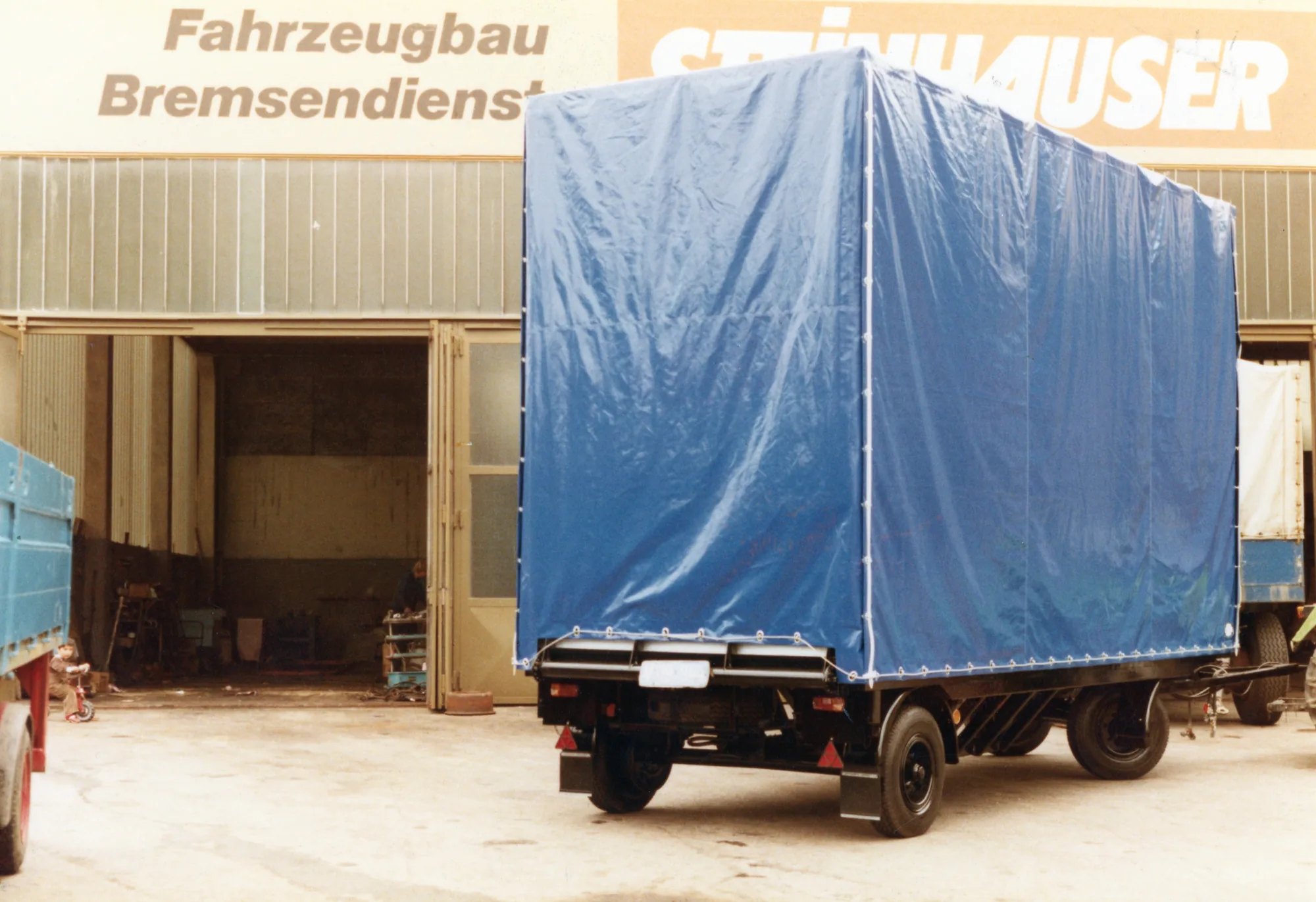 Anhänger mit blauem Planenaufbau vor der Steinhauser-Halle