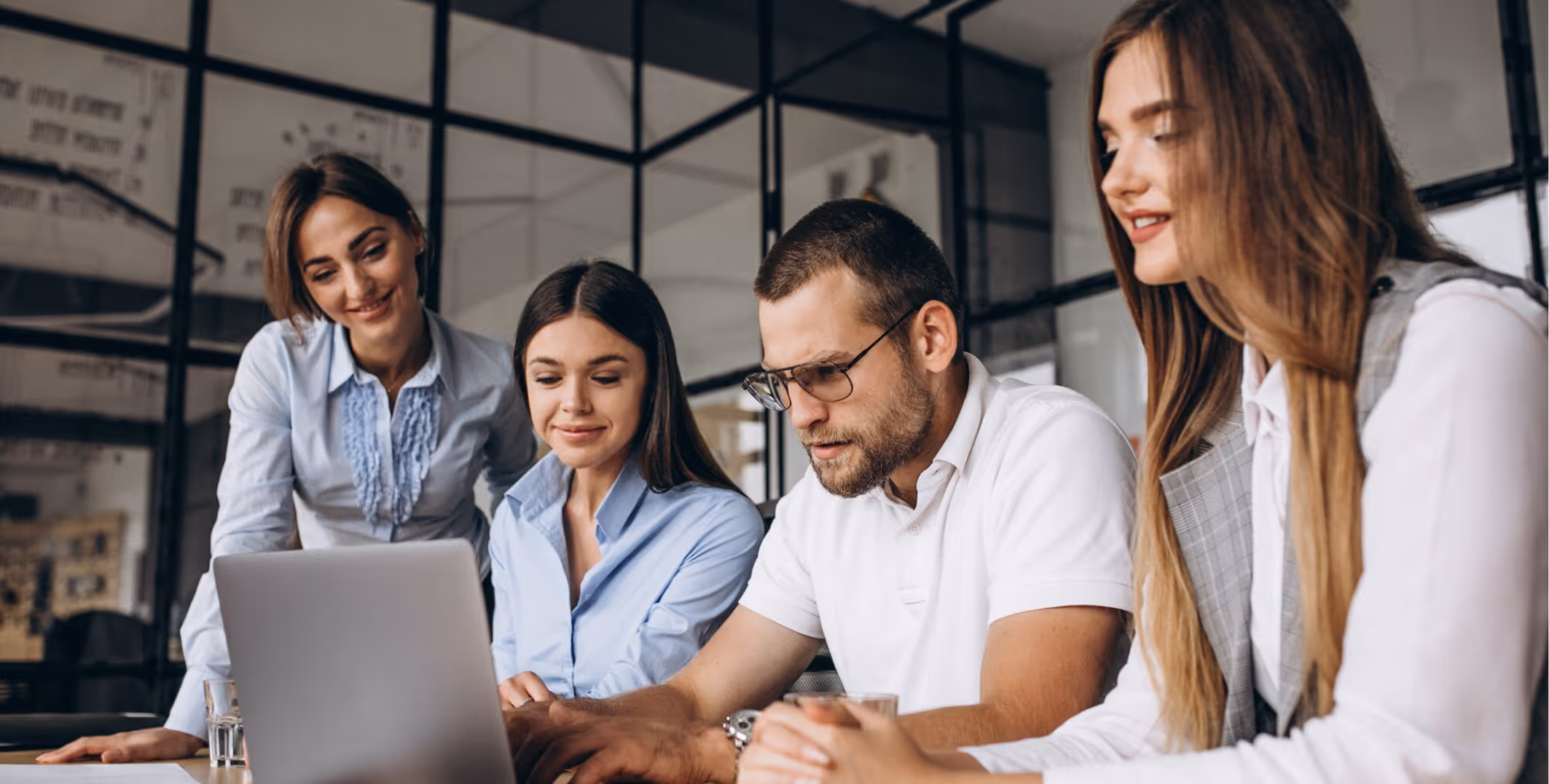 Four young professionals gathered around a laptop in a modern office, engaged in a discussion.