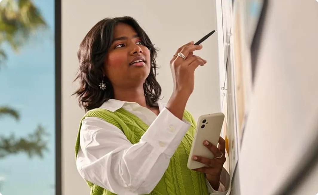 Woman taking notes on a whiteboard while holding a phone