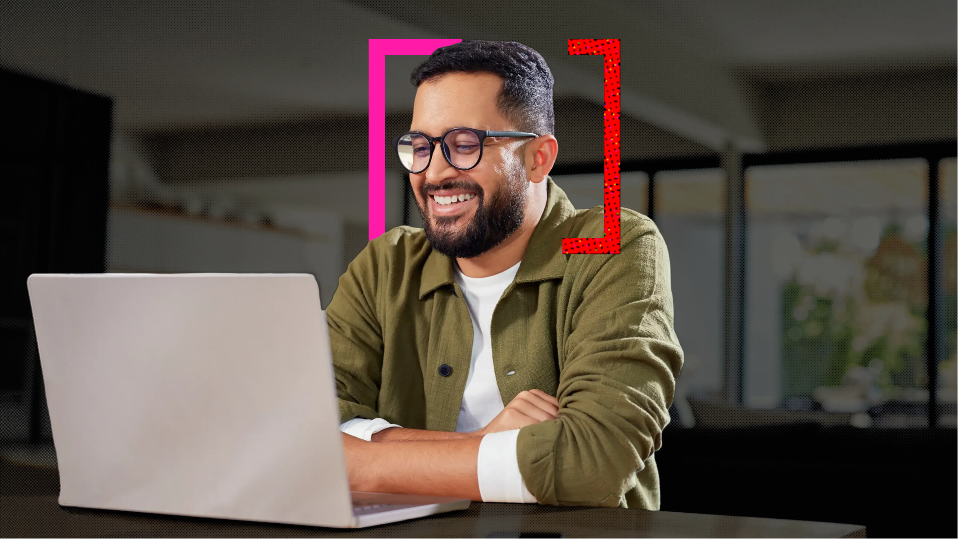 A man sitting at his desk looking and smiling at his laptop.