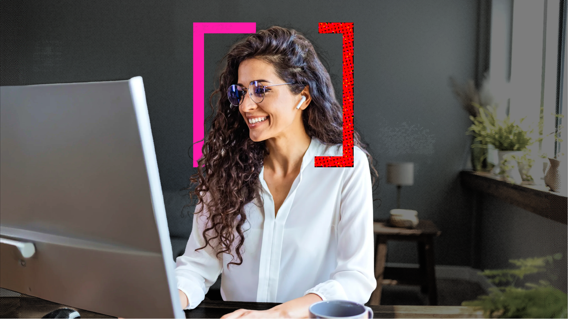 A woman, sitting at a desk, wearing earphones and glasses in a white shirt. She is sitting and smiling at her desk, looking at her computer monitor.
