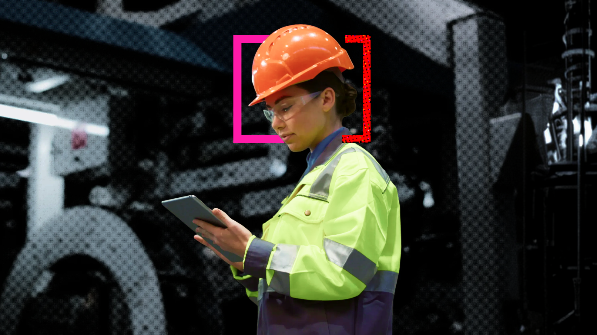 A frontline worker in a hard hat, safety glasses and high-visibility jacket checks a tablet on a factory floor.