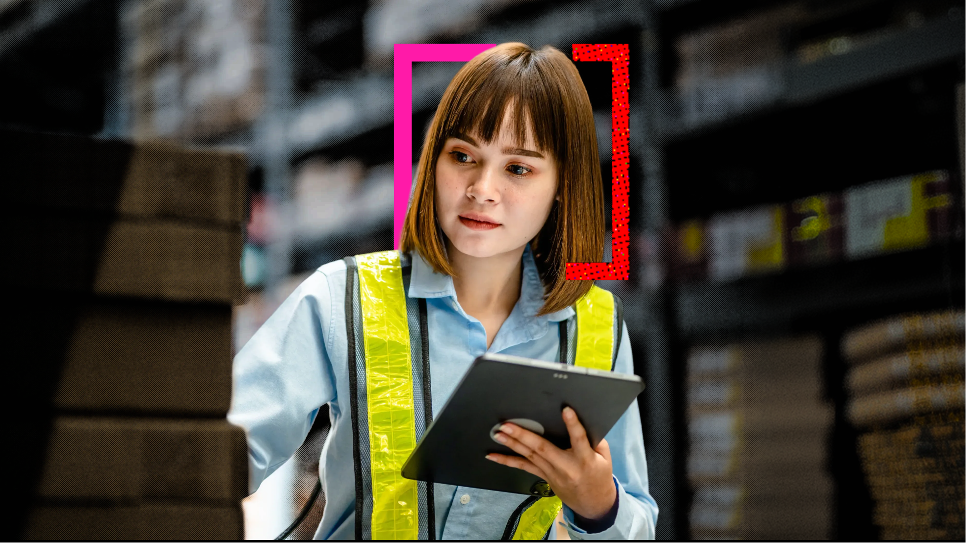 A woman in a high vis in a factory looking at her tablet and boxes.