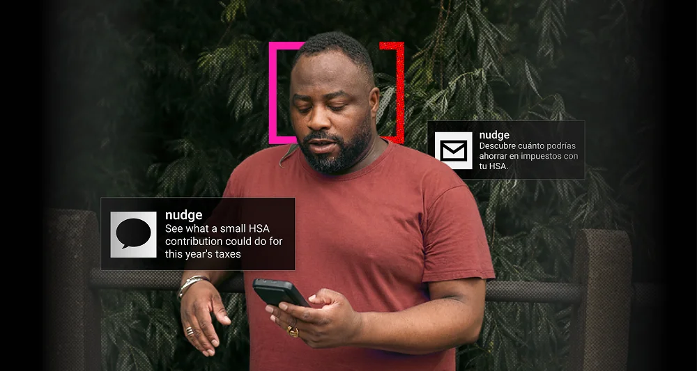 A man in a red t-shirt looks at a smartphone while standing outdoors near a wooden fence with dark green foliage in the background; two digital text boxes with the word 'nudge' appear beside him, one in English mentioning HSA contributions for taxes, and one in Spanish about saving on taxes with HSA.