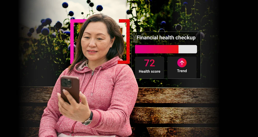 A woman in a pink jacket sitting on a wooden bench outdoors, looking at her smartphone, with a graphic overlay showing a financial health checkup score of 72 and an upward trend.