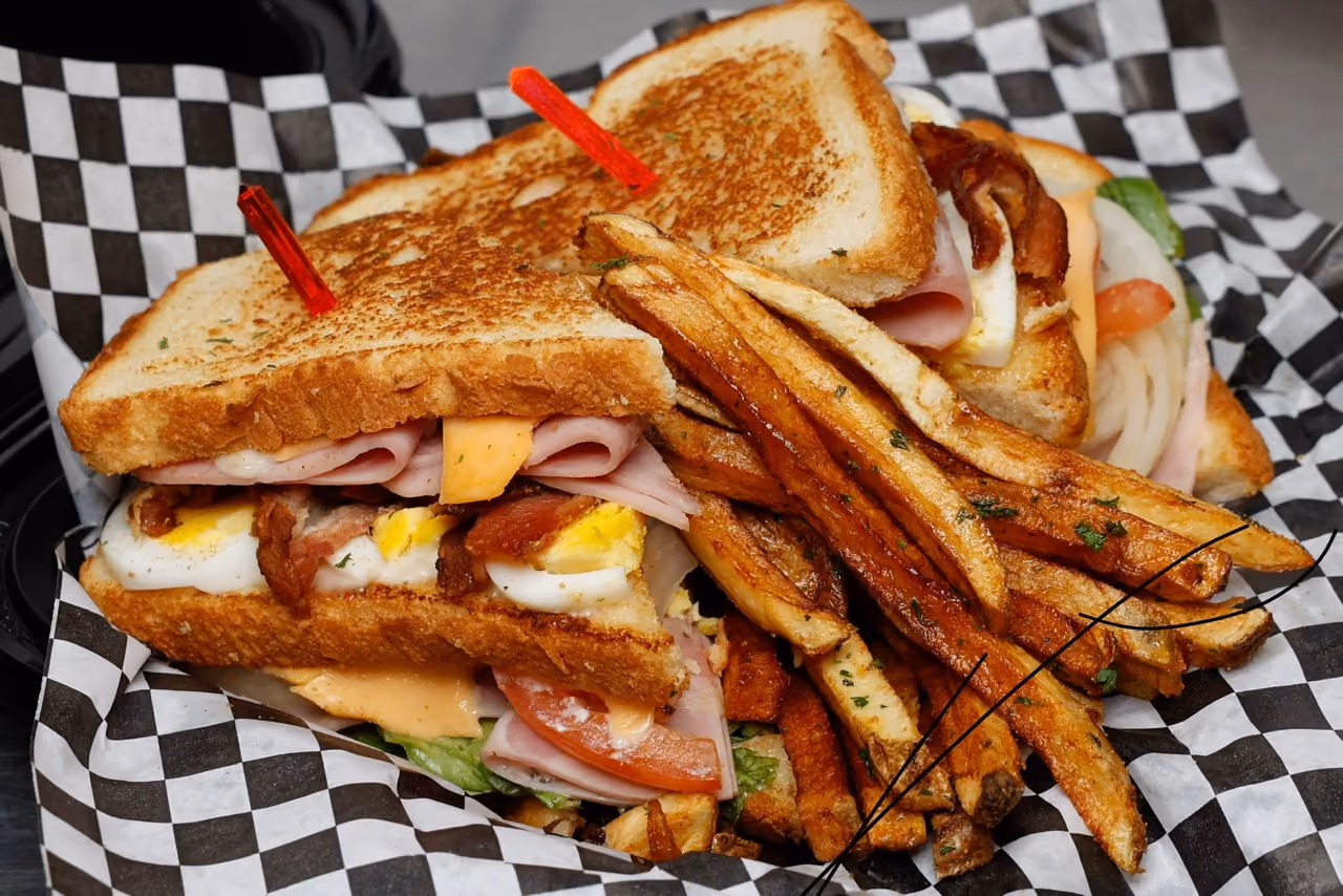 Double-decker sandwich with ham, egg, bacon, cheese, tomato, lettuce, served with seasoned fries.