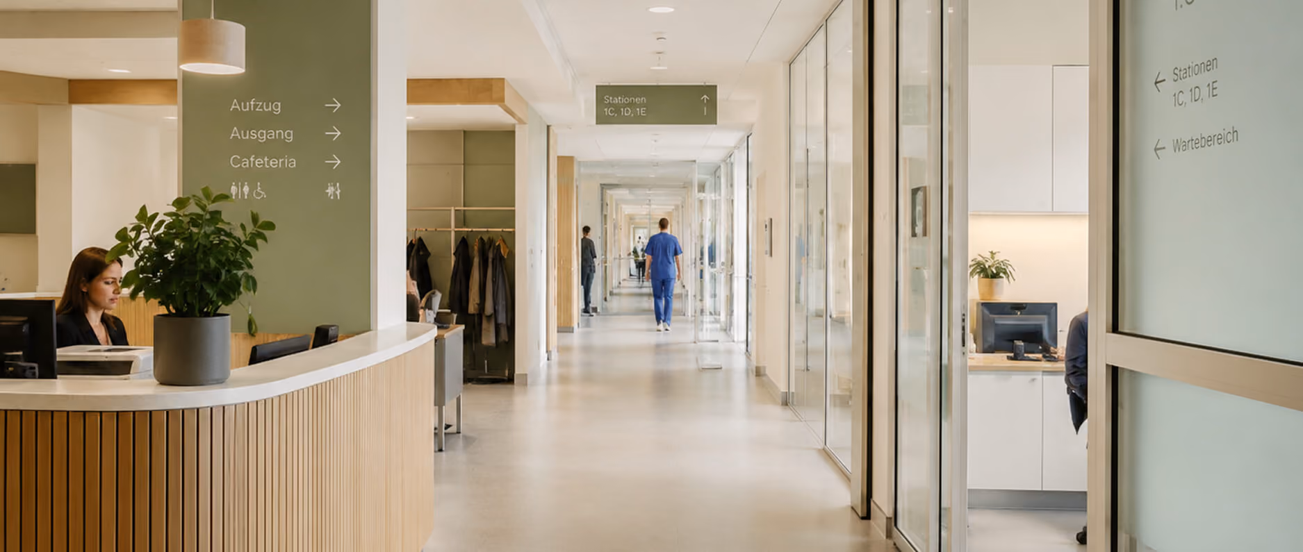 Modern hospital corridor with reception desk, staff in scrubs, and glass doors along the hallway.