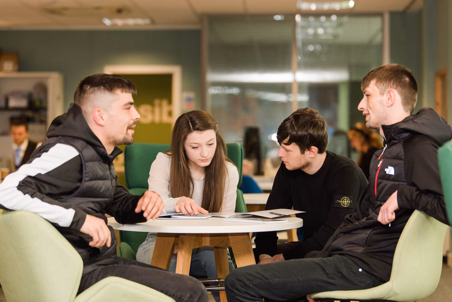 Four young adults seated around a round table looking at papers in a modern office space.