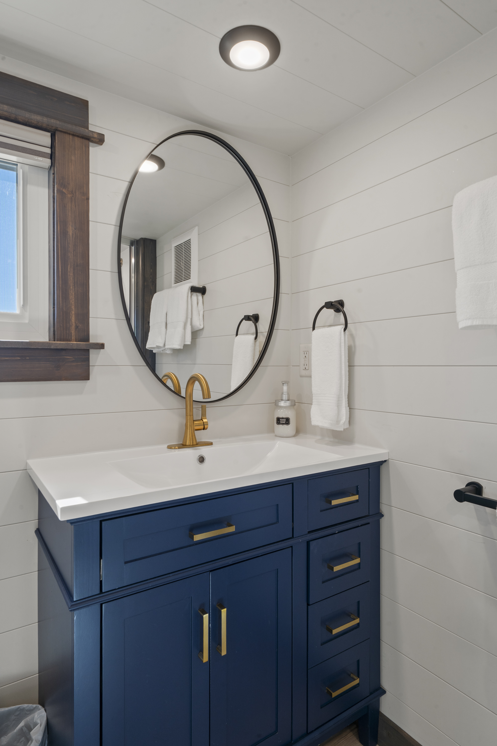 Royal Wulff bathroom with a navy vanity, brass faucet and round black mirror