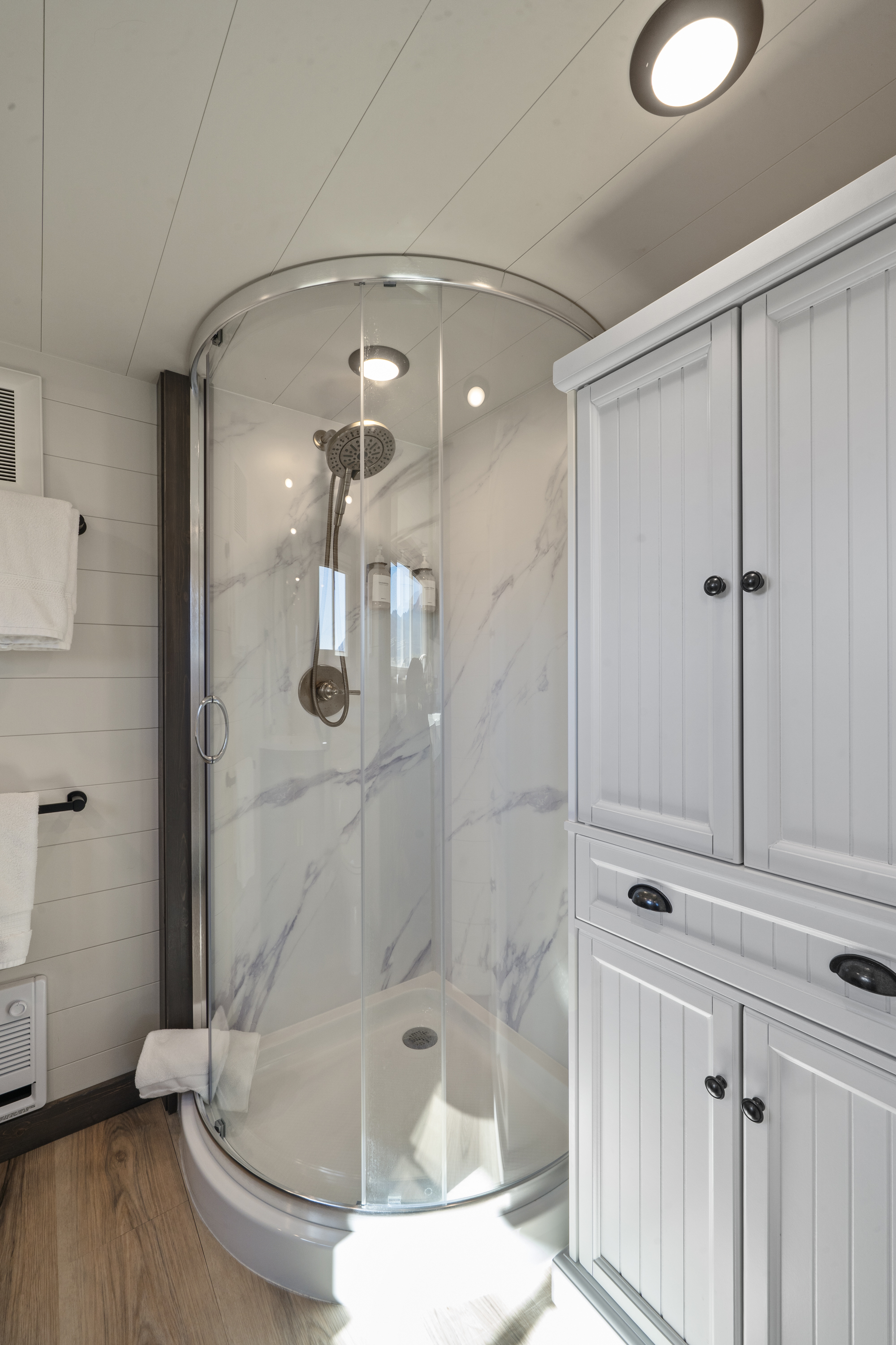 Royal Wulff curved glass shower with marble-look walls beside a white linen cabinet