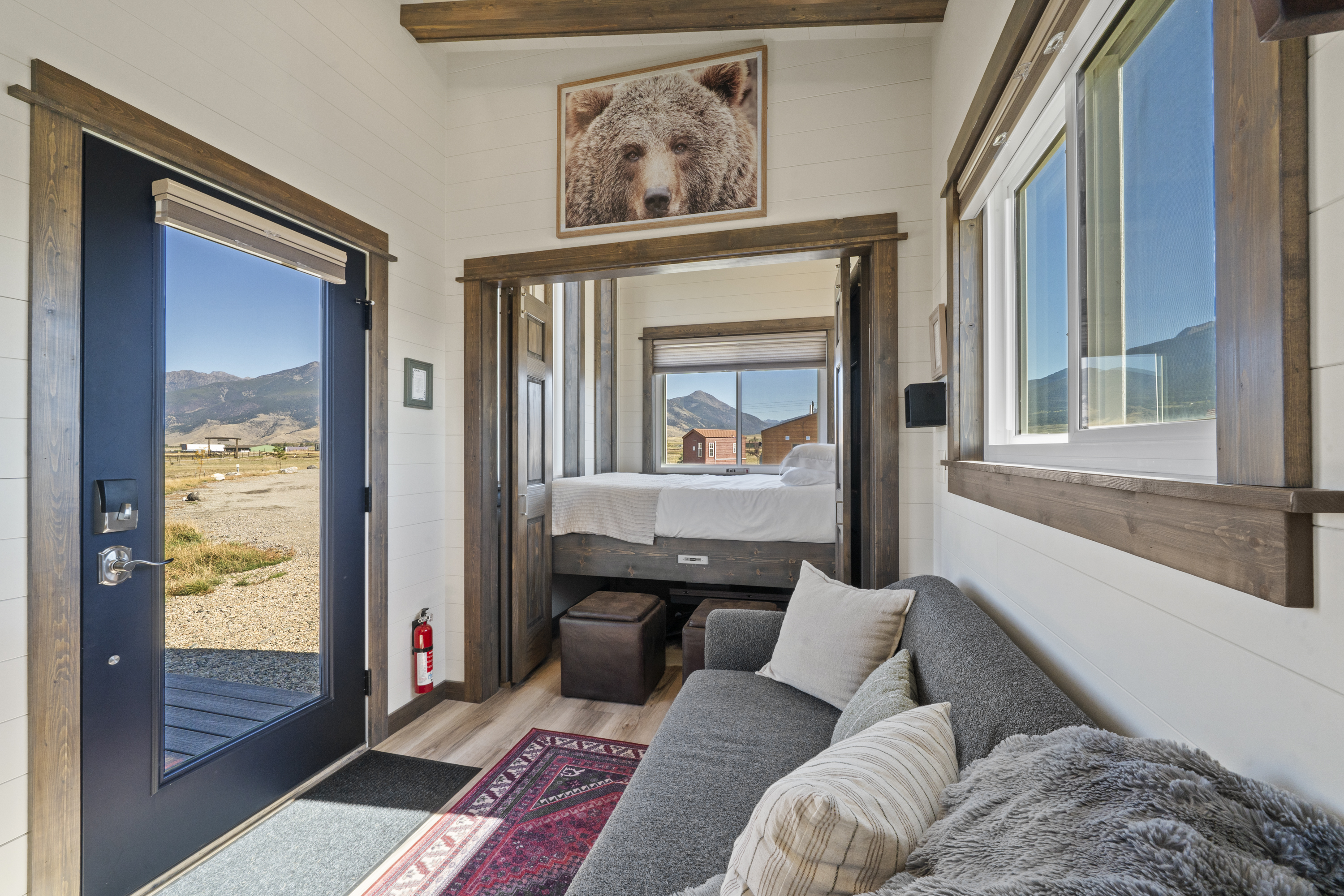 Royal Wulff living area with a gray sofa, a grizzly bear print, and the main-floor queen bed beyond, with mountain views out the windows