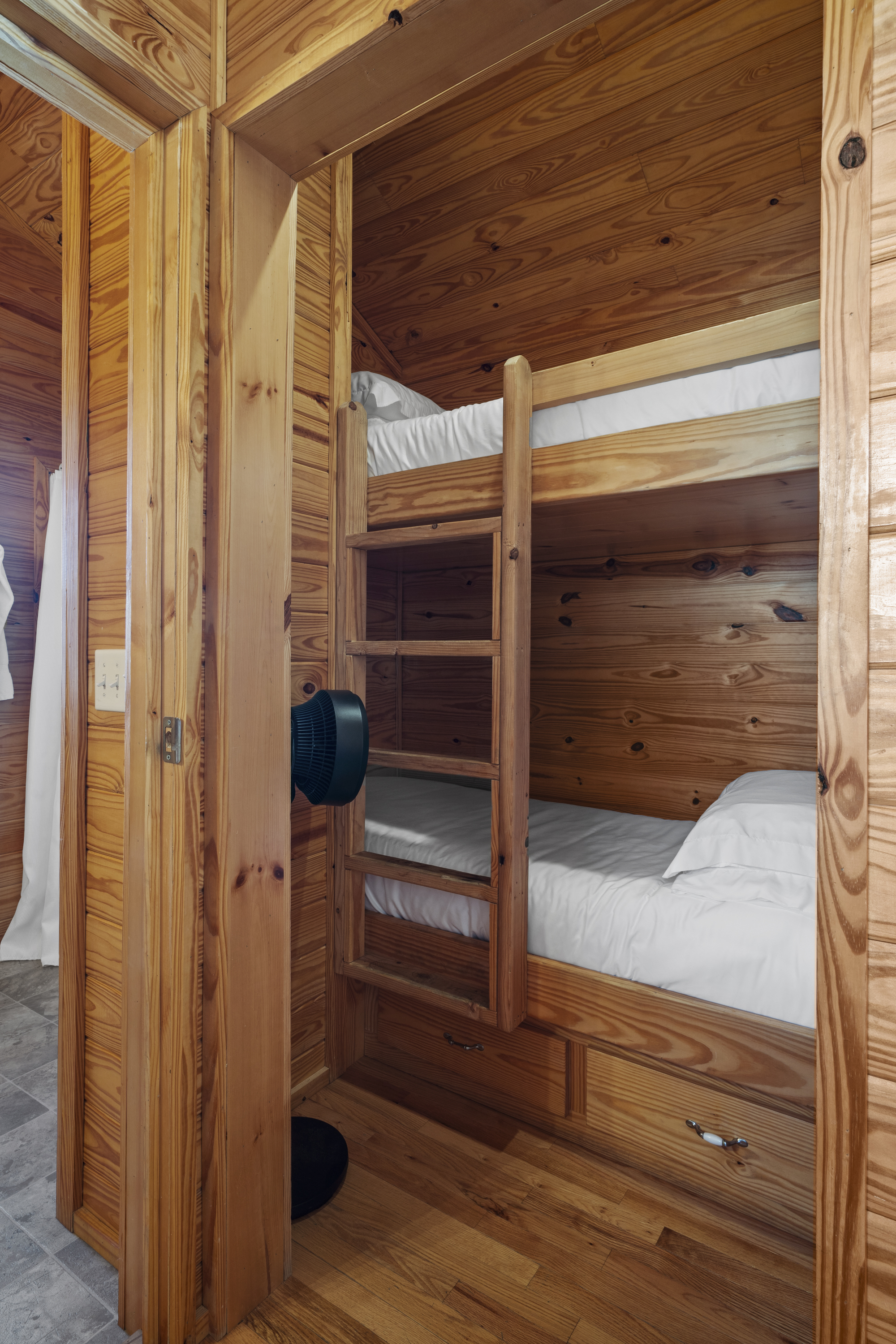 Pine bunk nook with two made-up bunks and a fan