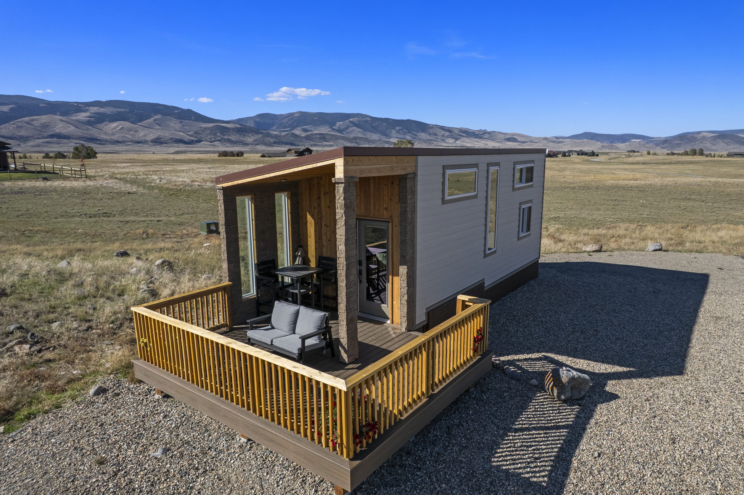 The Green Drake tiny home, with its covered porch and railed deck facing open range and mountains