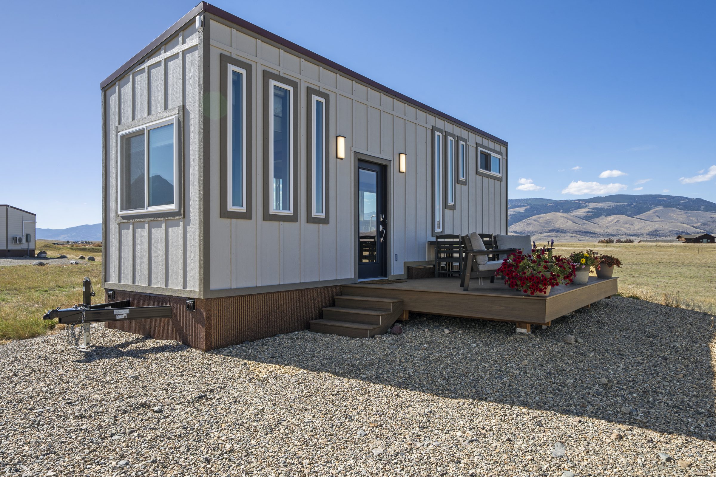 The Royal Wulff tiny home, with tall narrow windows and a deck set with chairs, a dining table and flowers
