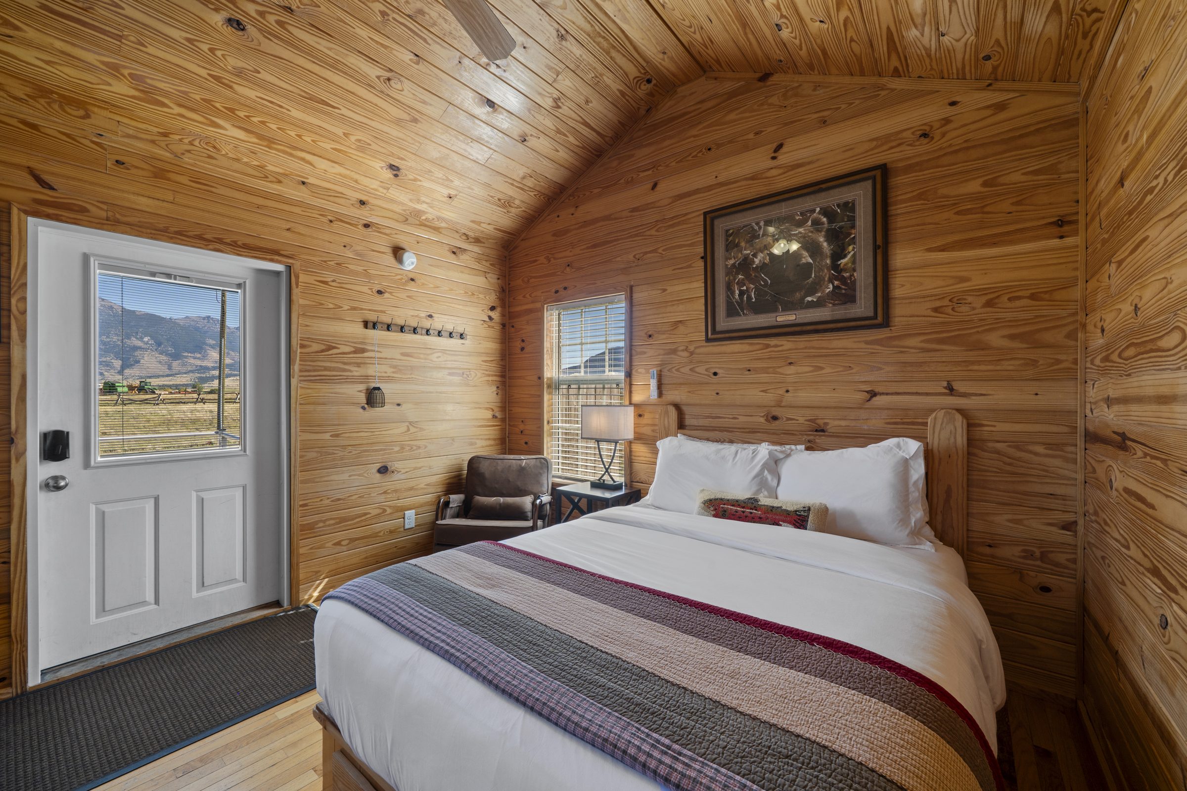 Queen bed with a trout pillow beside the cabin door, with mountains visible through the window