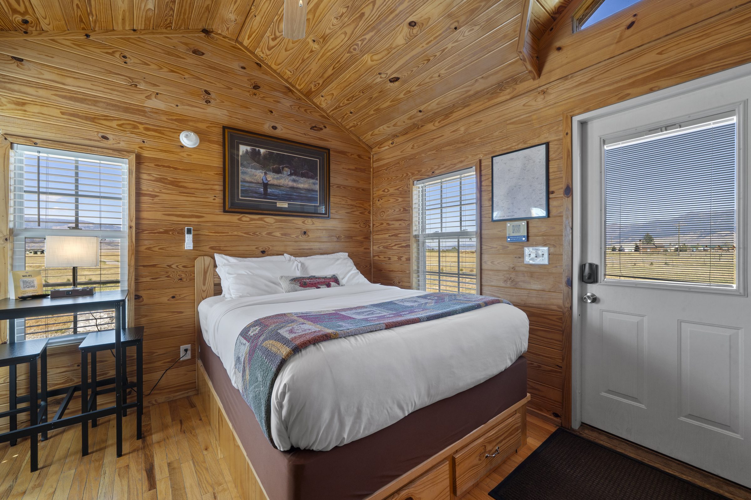 Cabin queen bed with a high-top table and stools, and windows on two sides