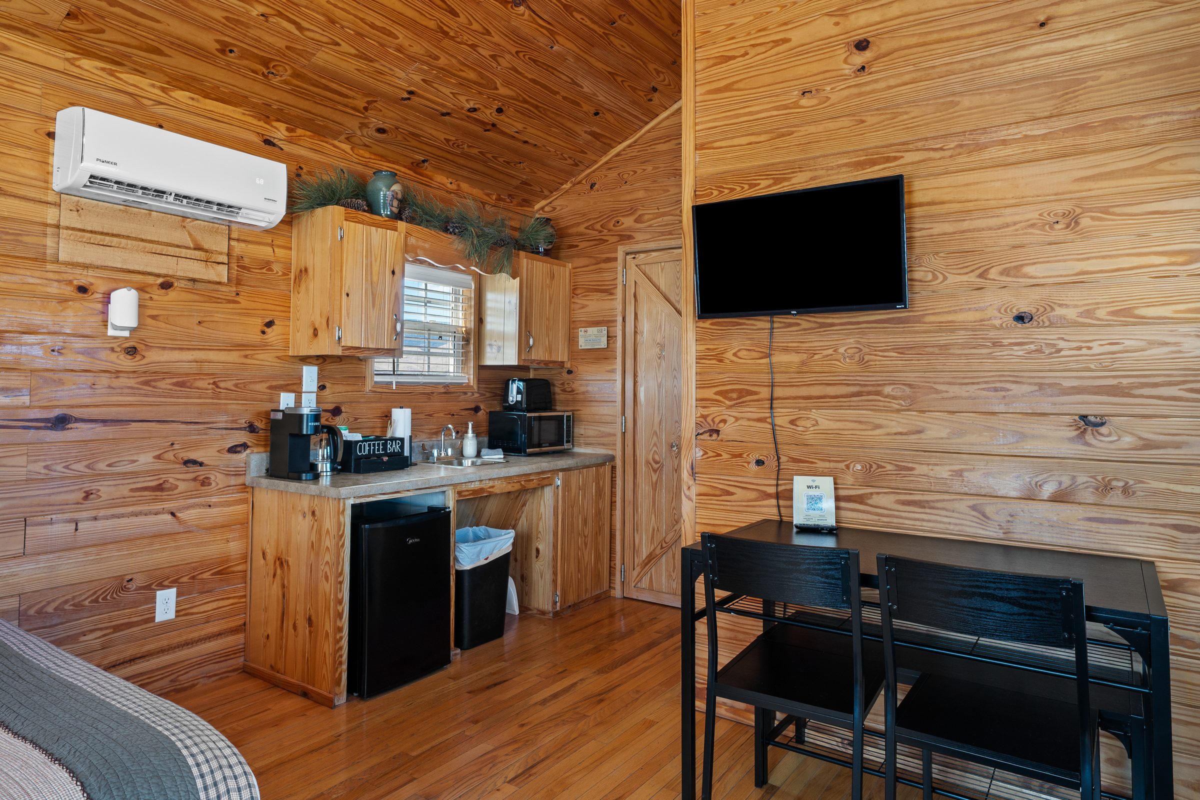 Cabin kitchenette with mini fridge, microwave and coffee maker, beside a dining table and wall-mounted TV
