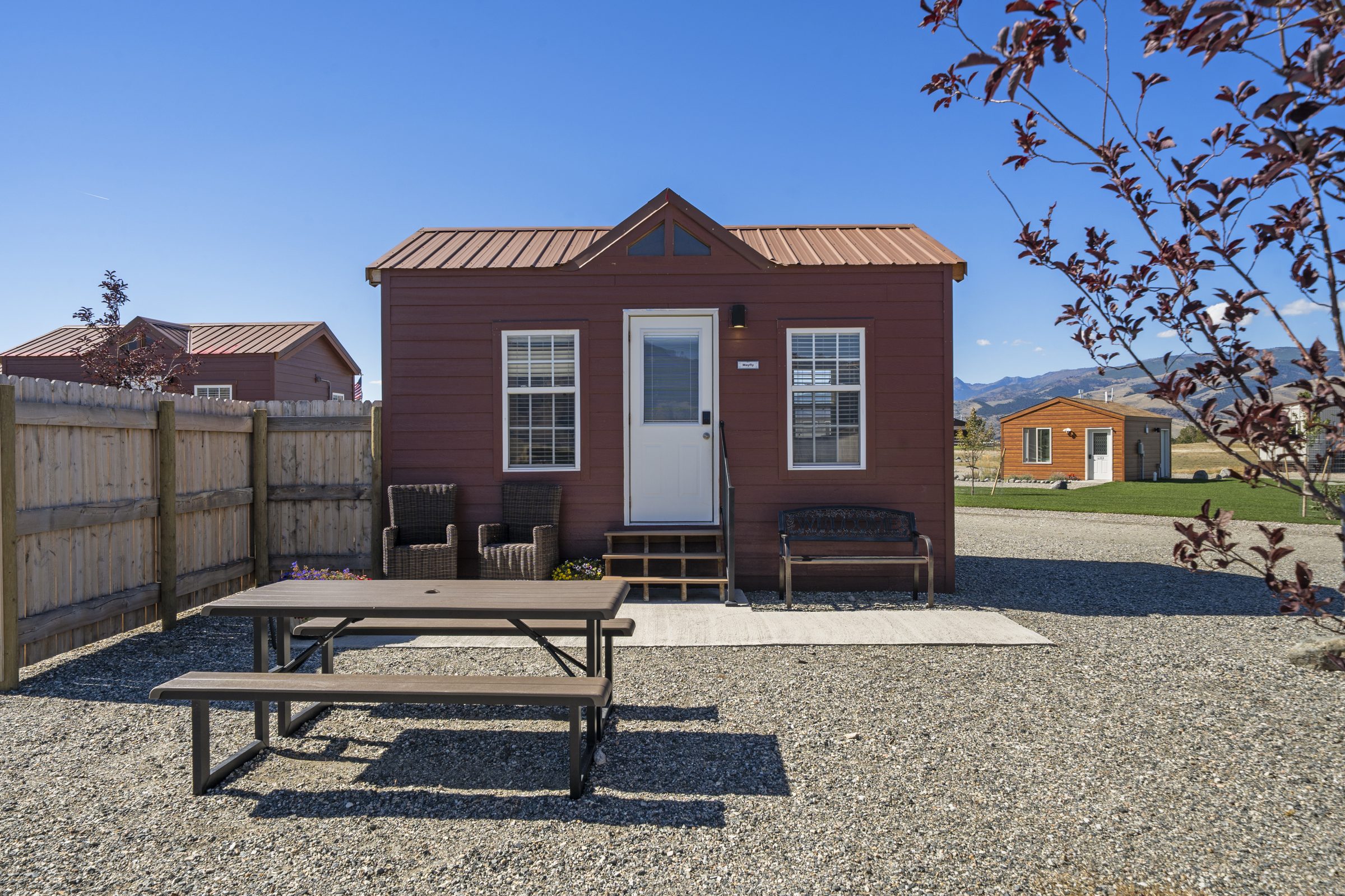 Mayfly Cabin, with a concrete patio, picnic table, two wicker chairs and a Welcome bench