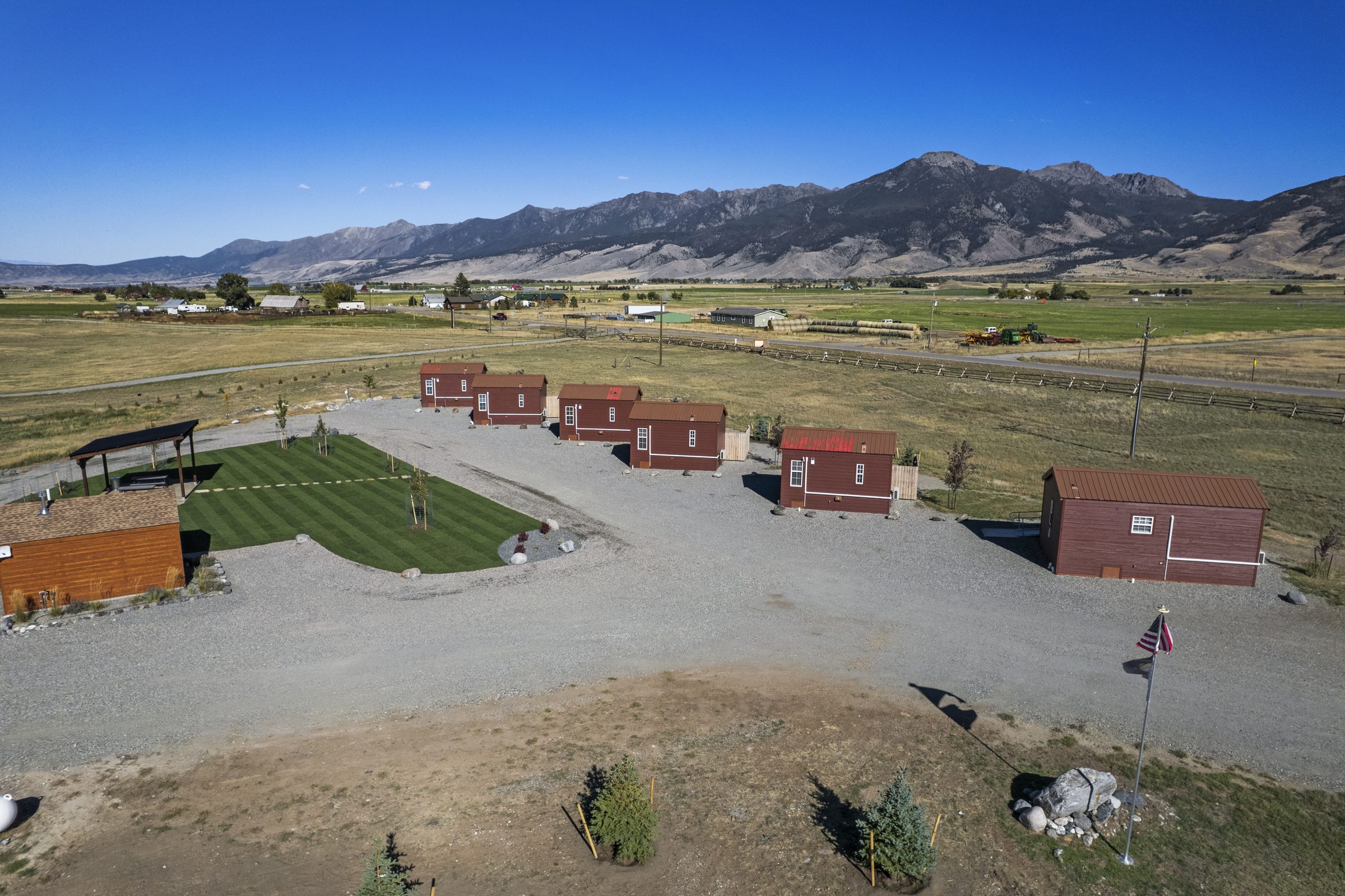 Aerial view of the six red cabins and the lawn, with rugged mountain peaks rising behind