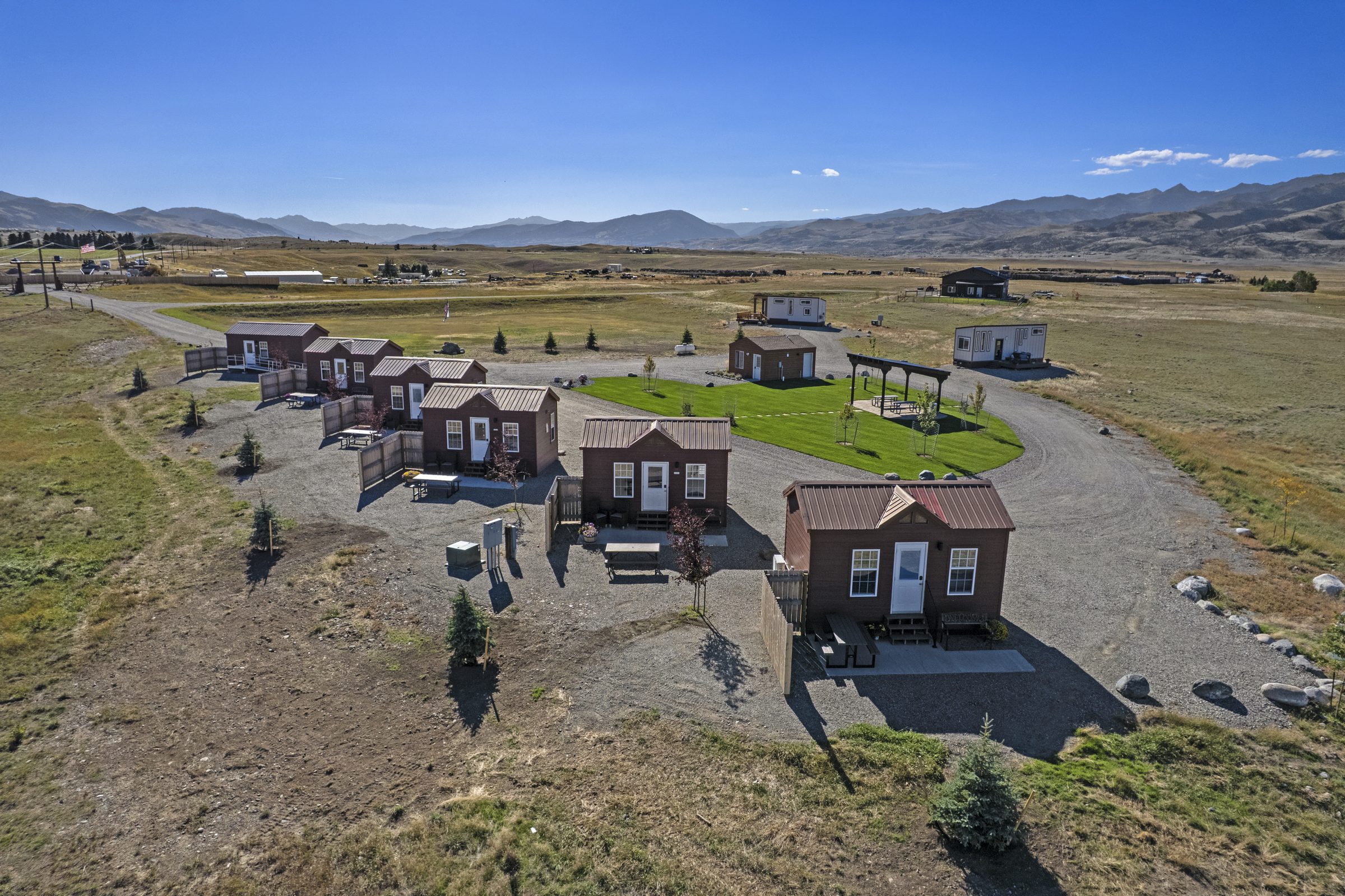 Aerial view of Yellow Stonefly Cabins: six red cabins, a lawn with a covered pavilion, and two tiny homes beyond, in Paradise Valley, Montana