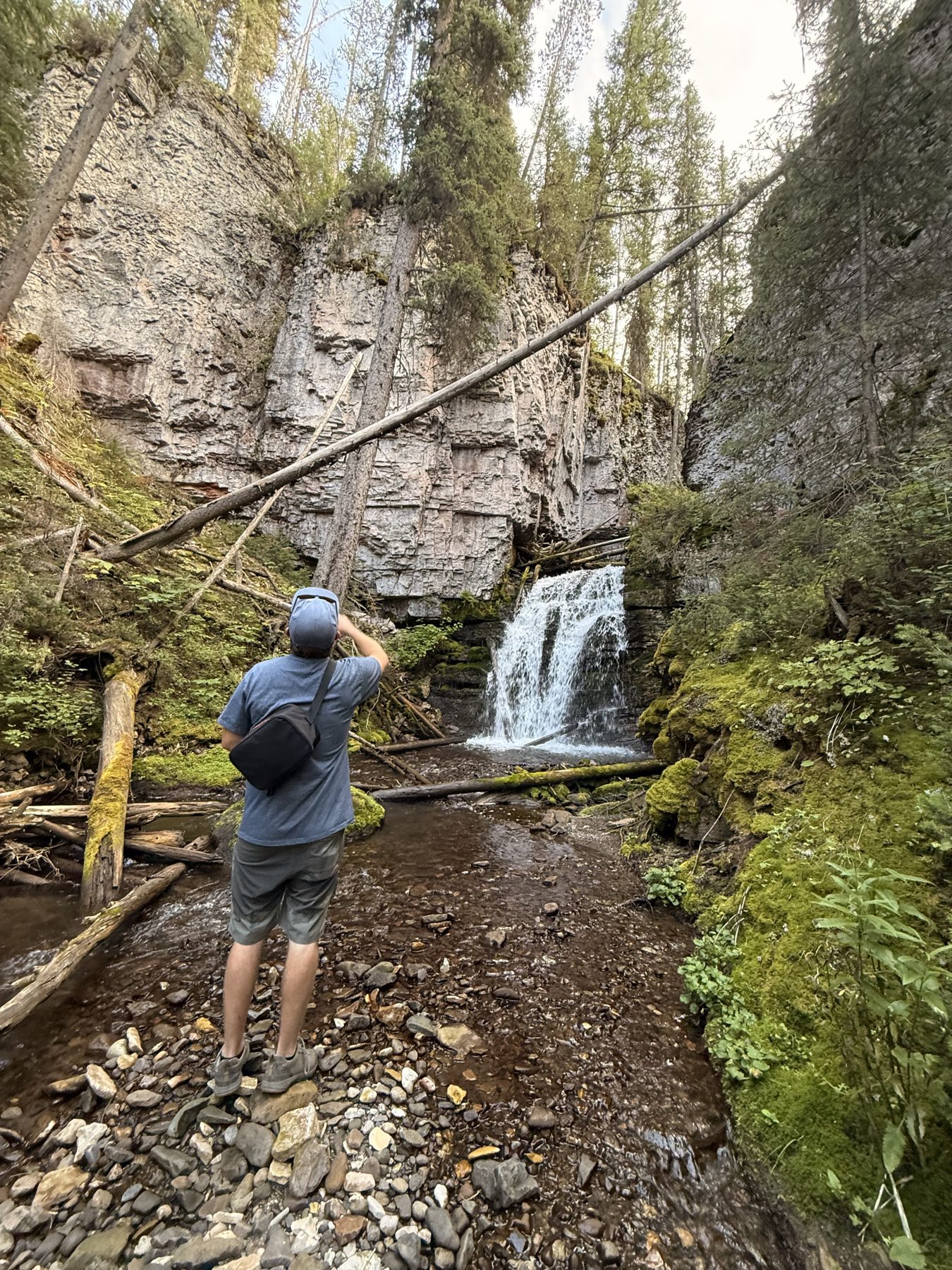 A hiker looking up at a waterfall in a narrow, mossy rock canyon