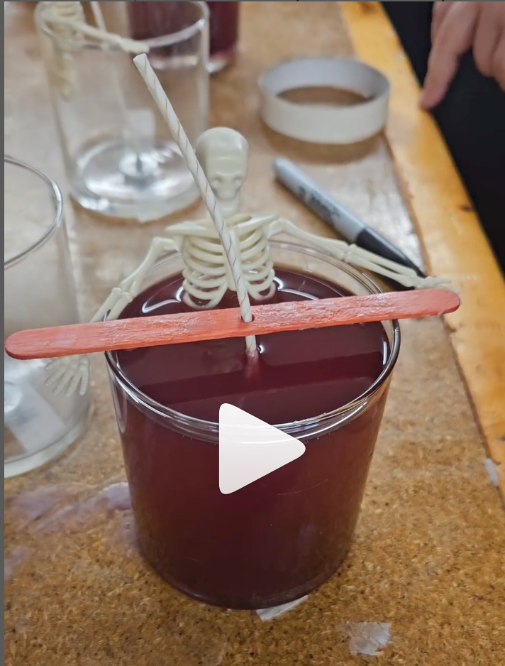 A skeleton toy sits in a red "bath of wax" in a candle vessel