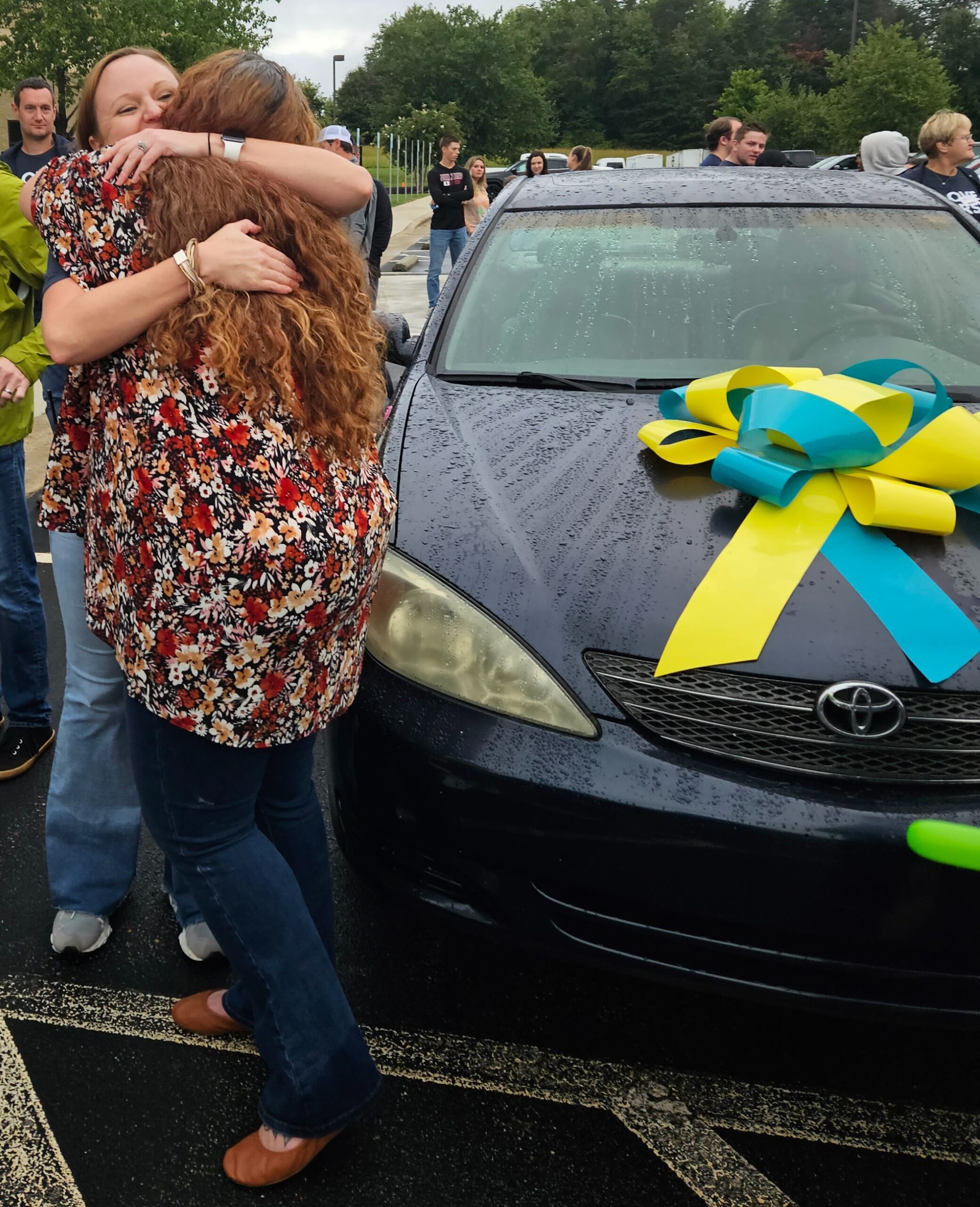 Two people hugging beside a car decorated with a bow