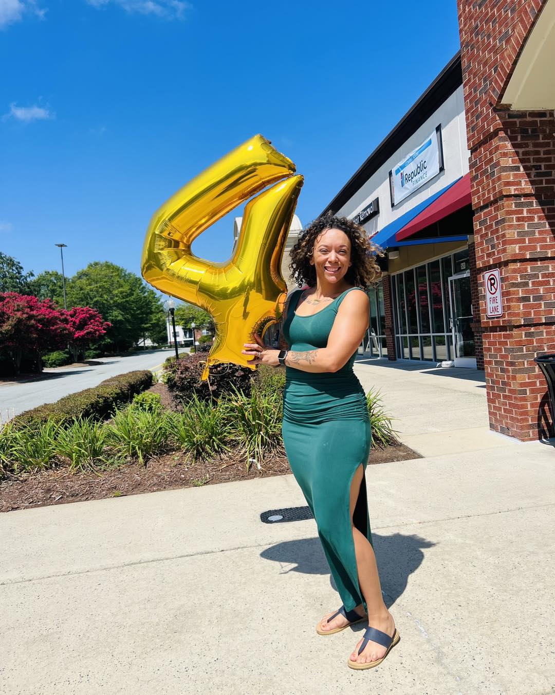 A person standing outside beside a gold number four balloon
