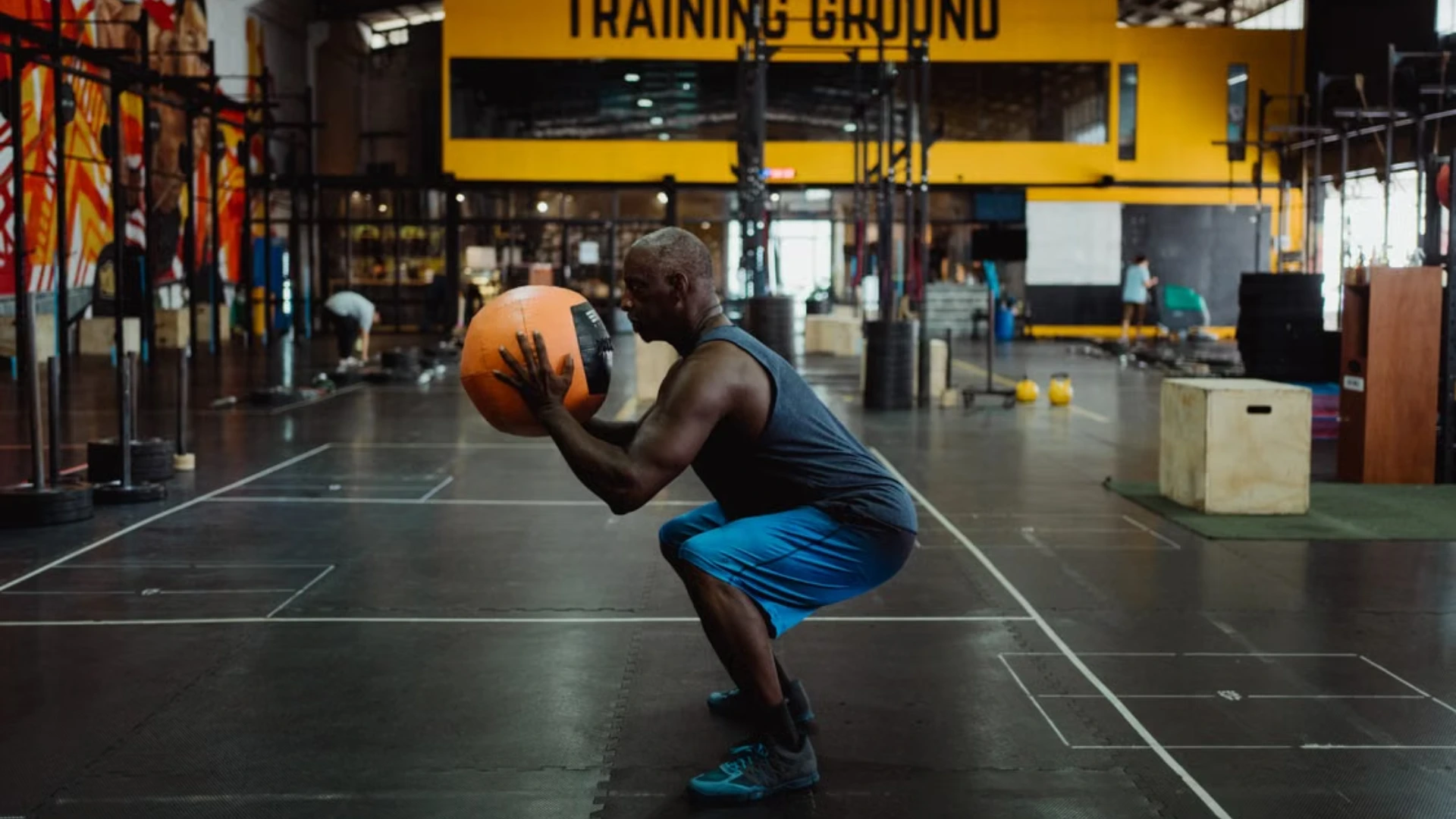 Man performing a medicine ball squat in a gym.
