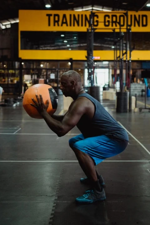 Man performing a medicine ball squat in a gym.