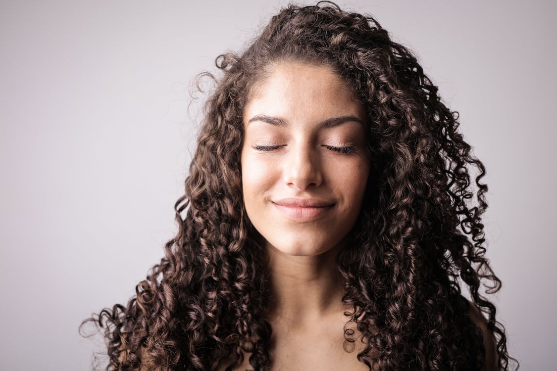 Close-up stock portrait of a smiling woman with curly hair and her eyes closed.
