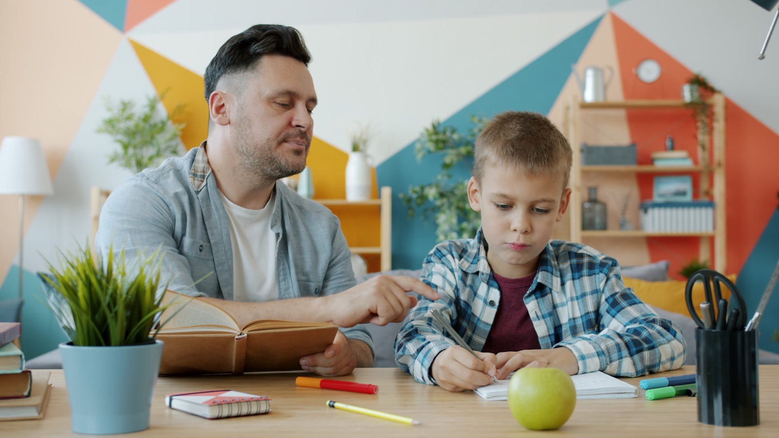 Un père aide son fils à faire ses devoirs à un bureau coloré
