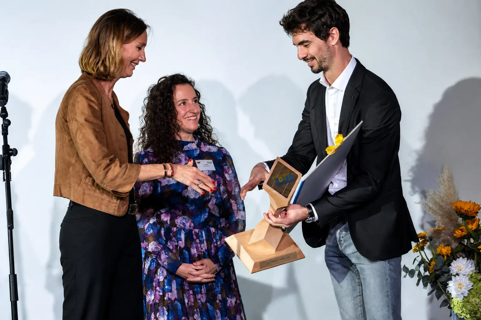 Preisübergabe am Schweizer Solarpreis, drei Personen auf der Bühne mit einer Trophäe