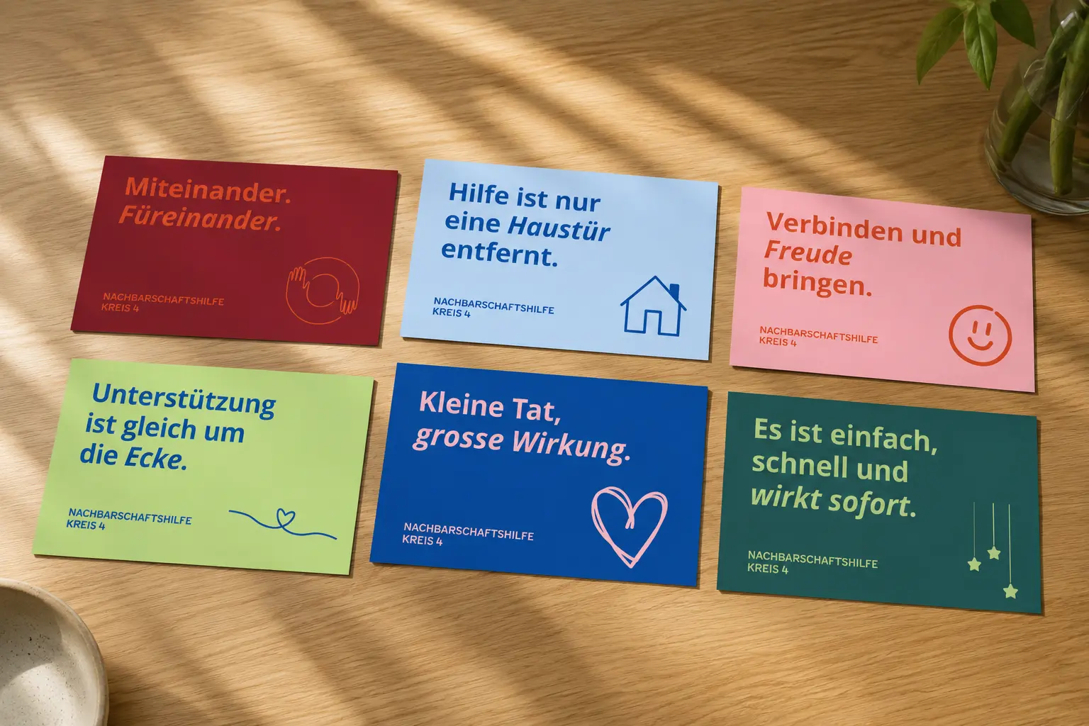 Sechs farbige Postkarten der Nachbarschaftshilfe Kreis 4 mit Claims wie «Kleine Tat, grosse Wirkung» auf einem Holztisch