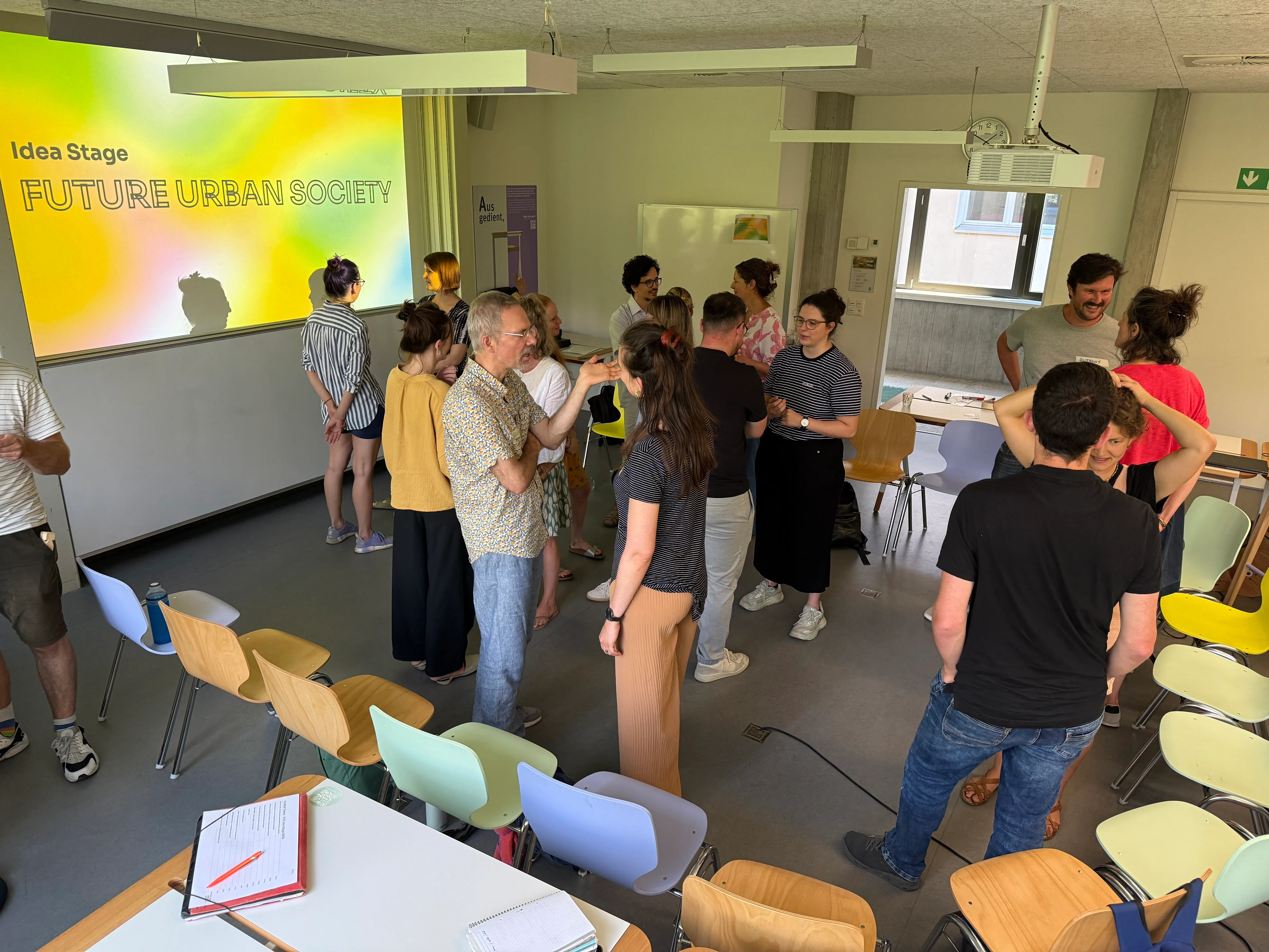 Teilnehmende im Austausch am Idea Stage Workshop von Future Urban Society, im Hintergrund die Projektion mit dem FUS-Logo