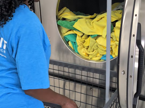 Staff member loading colored shop towels into a commercial washer