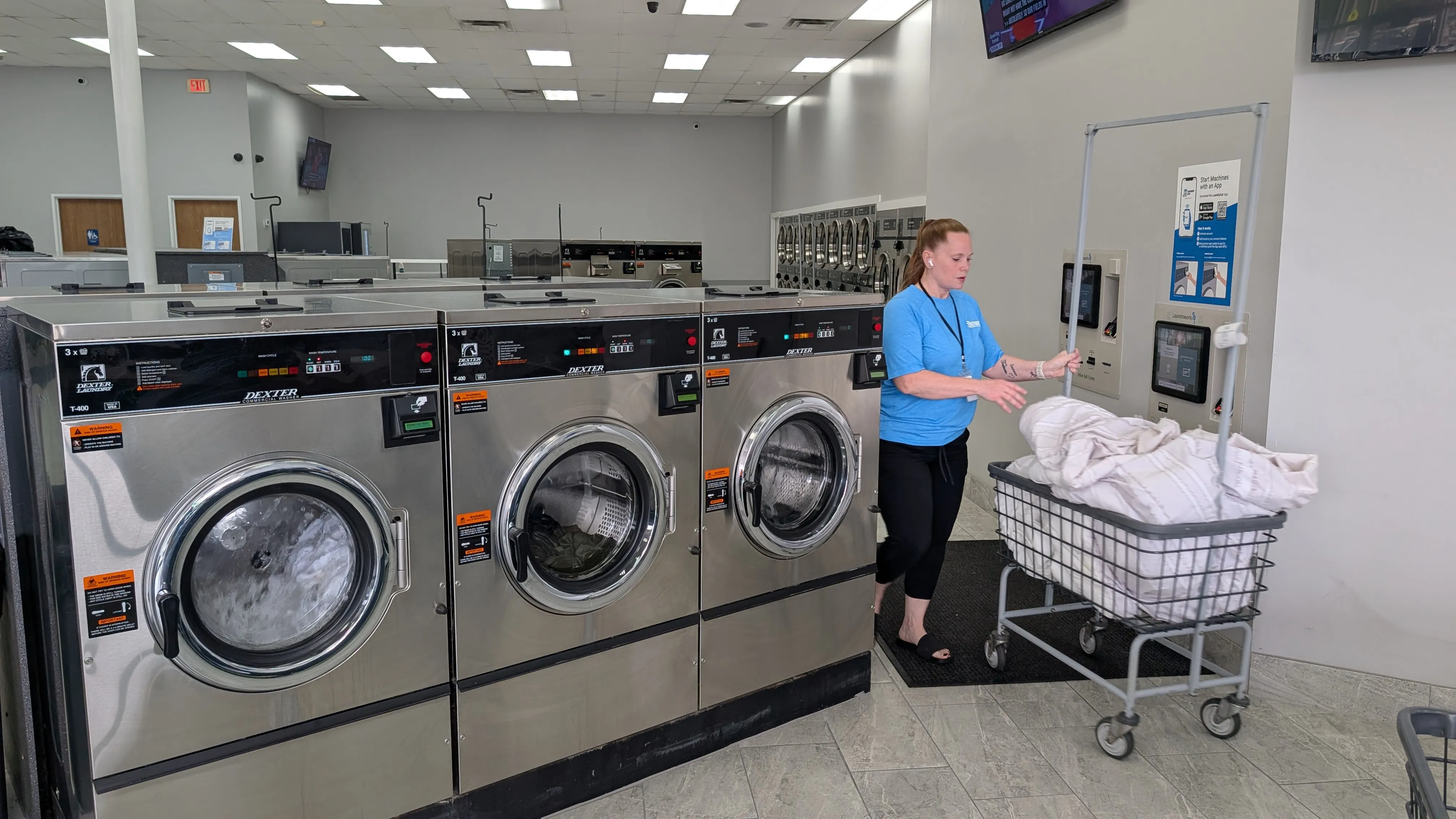 Attendant moving a cart of clean linens past the Dexter washers