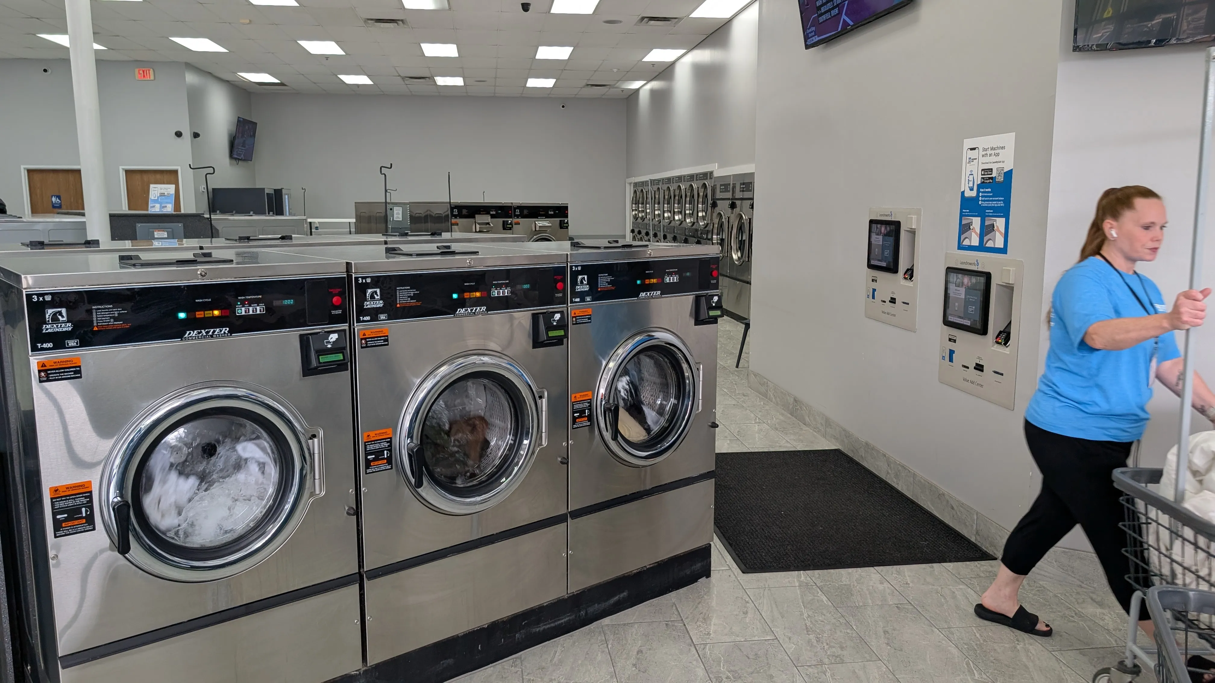 Attendant pushing a laundry cart past a row of Dexter washers